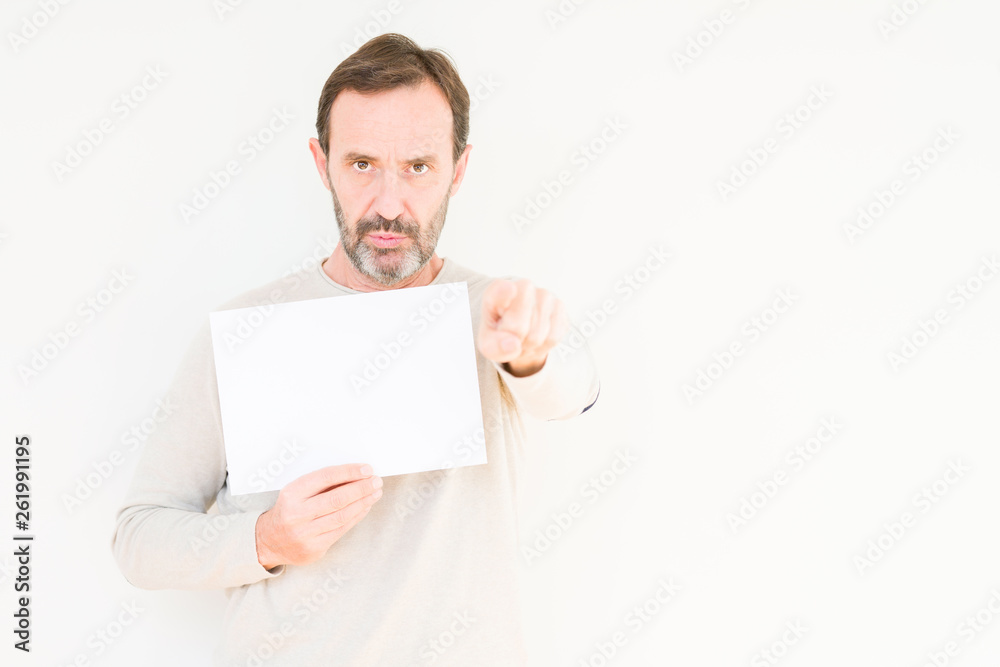 Senior man holding blank paper sheet over isolated background pointing with finger to the camera and to you, hand sign, positive and confident gesture from the front Senior man holding blank paper sheet over isolated background pointing with finger to the camera and to you, hand sign, positive and confident gesture from the front