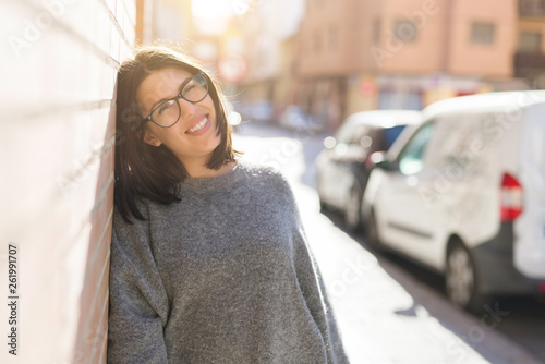 Beautiful young woman wearing glasses smiling cheerful leaning on bricks wall, casual pretty girl at the town