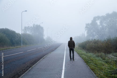 Young man alone walking on sidewalk in mist of early morning. Foggy air. Go away. Back view.