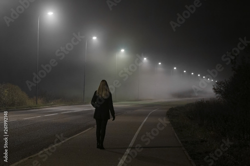 Fotografie Young woman alone slowly walking under white street lights in night