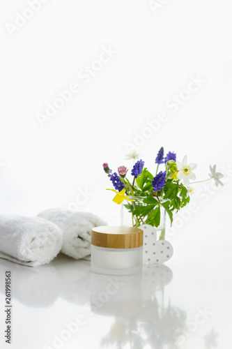 handtücher neben einer Cremedose vor weißem Hintergrund und Blumen in einer Vase.