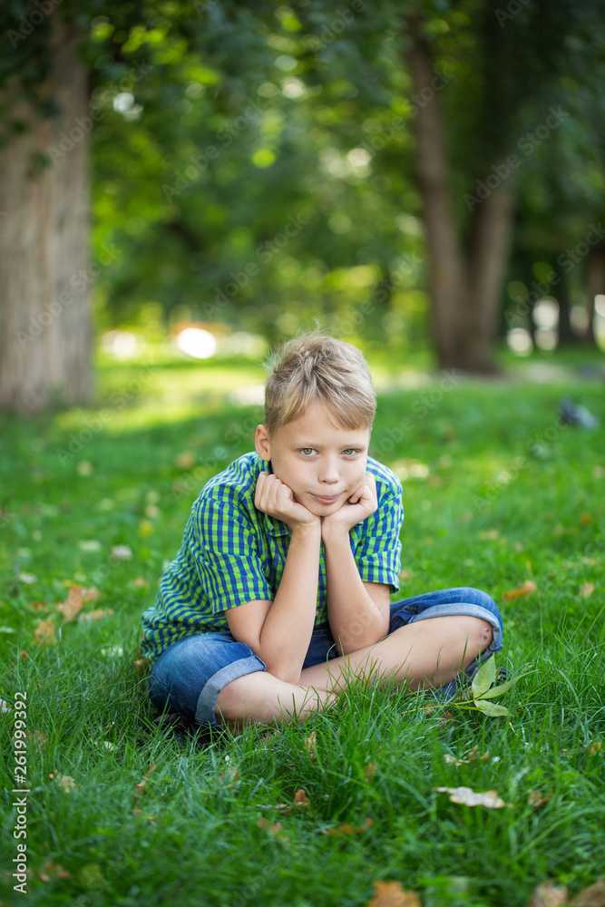 Vertical photography of white kid sitting on green grass outdoors at urban park. Vertical photography of white kid sitting on green grass outdoors at urban park.