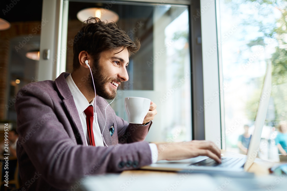 Fototapeta premium Young man at cafe drinking coffee and working on laptop