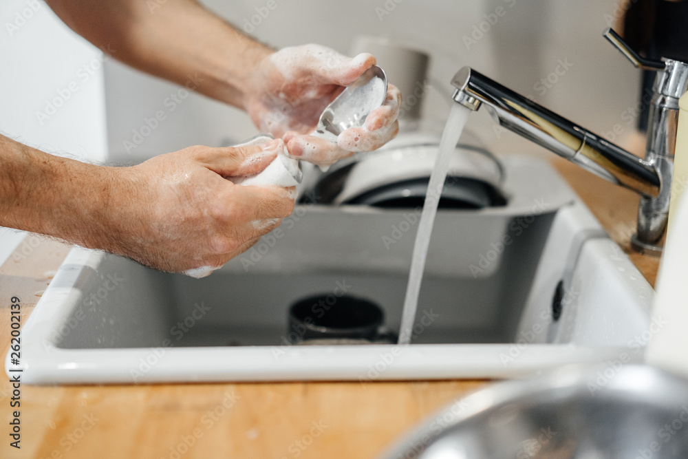Homework, male hands with a sponge in the foam wash spoons in the sink in the kitchen detergent. Homework, male hands with a sponge in the foam wash spoons in the sink in the kitchen detergent.