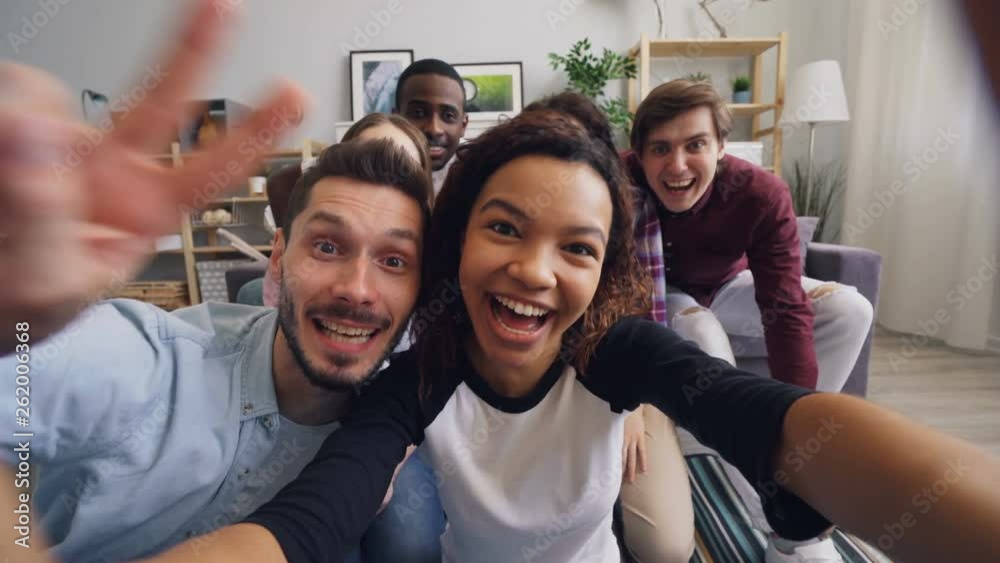 POV of happy youth men and women making online video call at home waving hand talking looking at camera and laughing. Modern technology and communication concept.