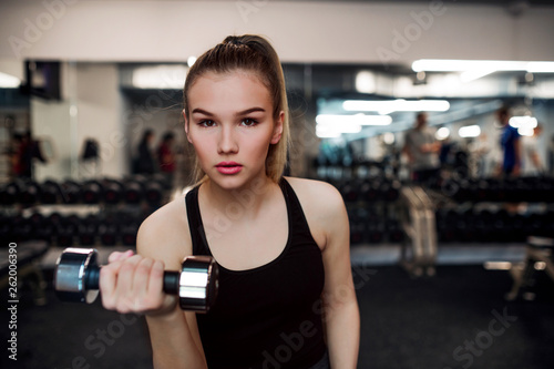 Young girl or woman with dumbbells, doing workout in a gym.