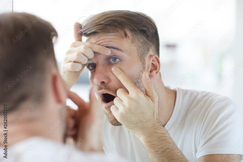 Portrait of handsome young man checking eyes looking at his reflection in mirror, copy space Portrait of handsome young man checking eyes looking at his reflection in mirror, copy space