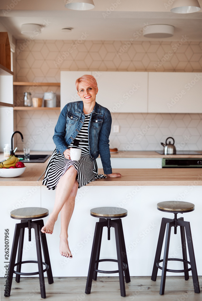 Naklejka premium A young attractive woman sitting on a counter in a kitchen at home.