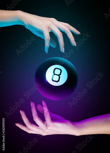 Hands with magic billiard ball number eight on a dark background. Cyan and purple light