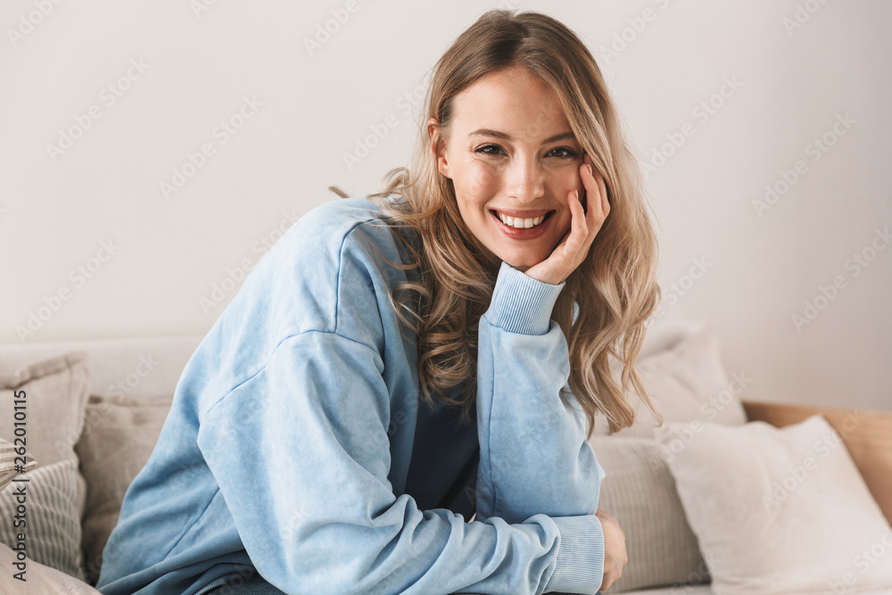 Portrait of gorgeous blond girl smiling and looking at camera while sitting on sofa at home Portrait of gorgeous blond girl smiling and looking at camera while sitting on sofa at home