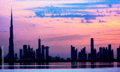 Stunning view of the silhouette of the Dubai skyline during sunset with the magnificent Burj Khalifa and many other buildings and skyscrapers reflected on a silky smooth water. Dubai.