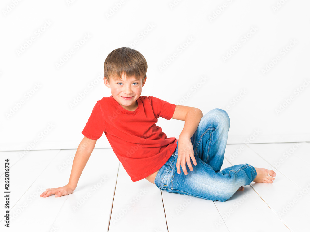 stille hinanden embargo cute and blond boy with red shirt and blue jeans is posing on white wooden  floor in front of white background Stock Photo | Adobe Stock