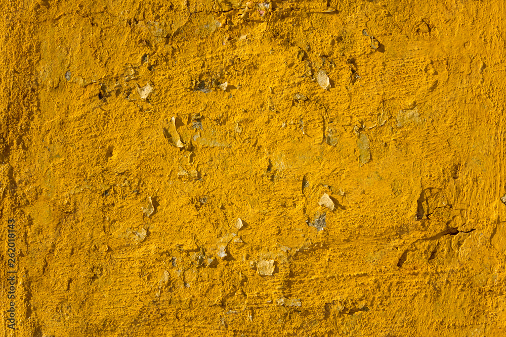 an old shabby bright yellow wall with deep relief, scraps of paper and cracks with shadows. rough surface texture an old shabby bright yellow wall with deep relief, scraps of paper and cracks with shadows. rough surface texture