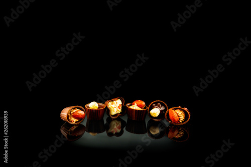 Chocolate candies with broken chocolate pieces on black reflective background. Space for text