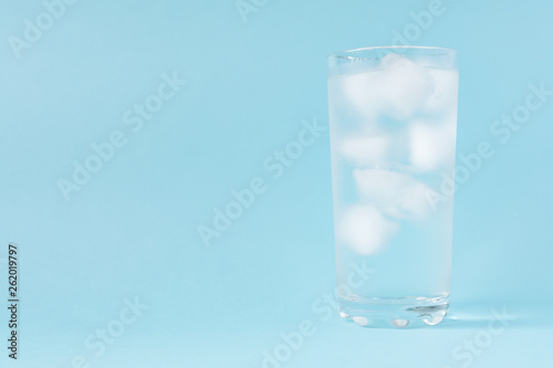 Close up of pure water with ice in tall transparent glass with copy space on blue background.
