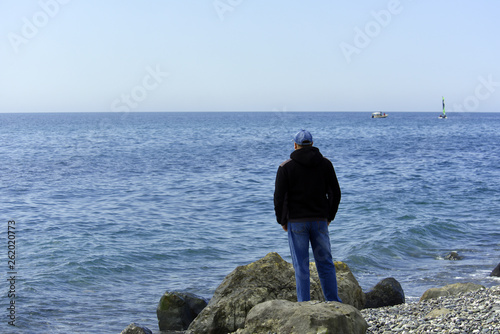 A man stands on a stone and looks at the sea
