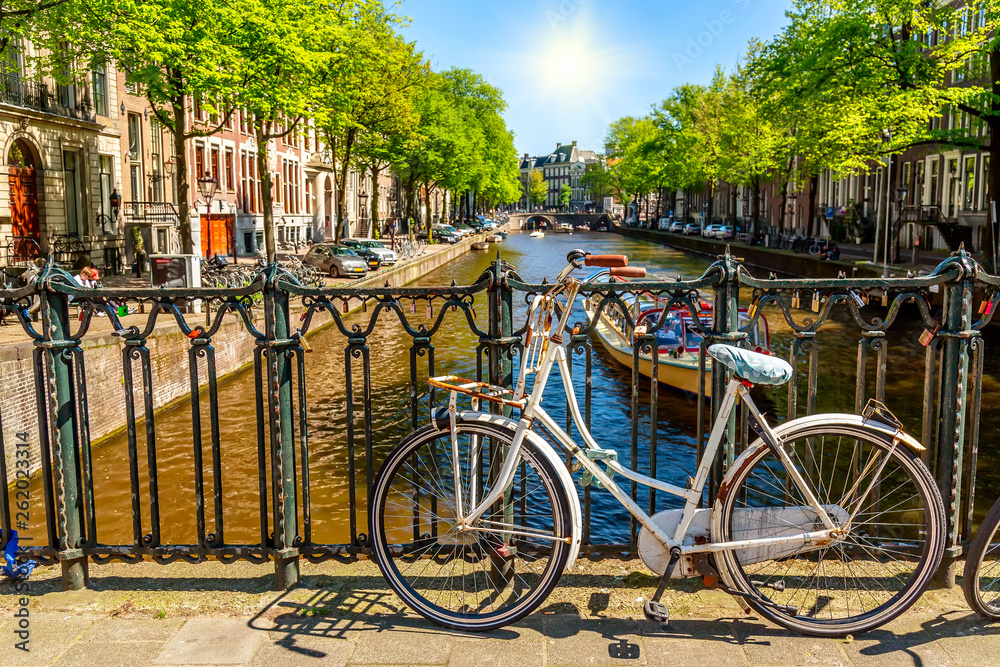 Old bicycle on the bridge in Amsterdam, Netherlands against a canal during summer sunny day. Amsterdam postcard iconic view. Tourism concept.