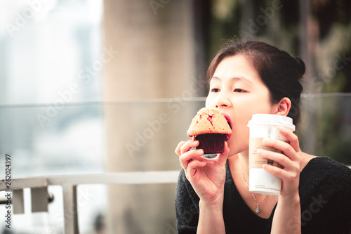 Young woman drinking coffee and eating a delicious muffin cake in cafe 