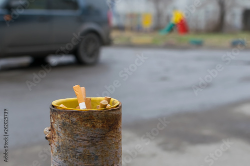 cigarette butts are stored in a pipe of a column protection for the Parking which is about the road in the background a Playground photo