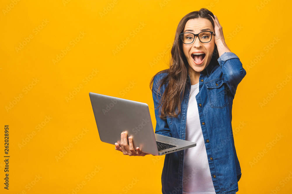 OMG! I'm shocked! Portrait of a shocked young beautiful girl holding laptop computer isolated over yellow background. OMG! I'm shocked! Portrait of a shocked young beautiful girl holding laptop computer isolated over yellow background.