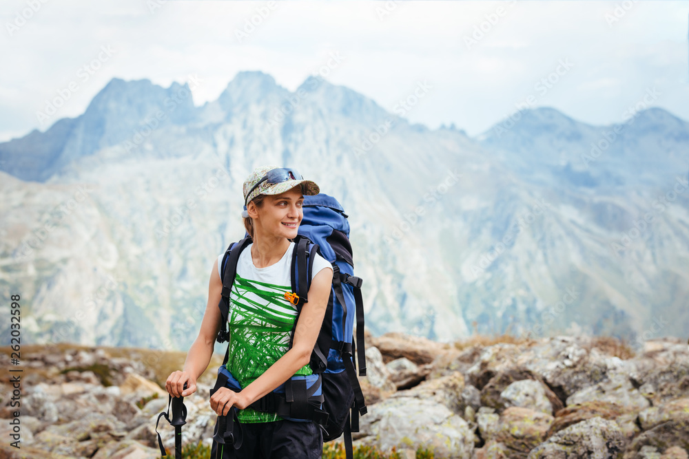 Young female tourist with backpack in the mountains smiling. Looking to the side. The concept of active lifestyle and health. Copy space for text.