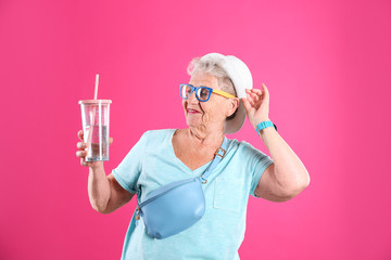 Portrait of cool grandmother with drink on color background