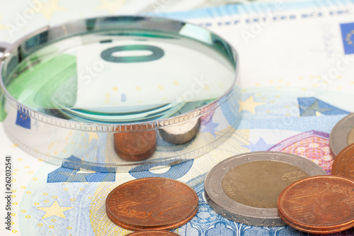 Magnifying glass and many euro bills and coins Limited depth of field