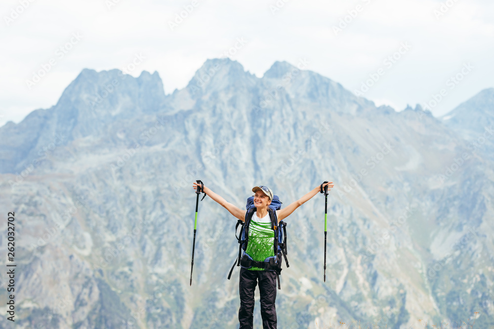 Joyful happy beautiful young woman-tourist with a backpack in the mountains. Copy space for text