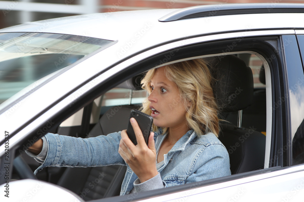 Frau hält während des Autofahrens ein Handy in der Hand und schaut entsetzt