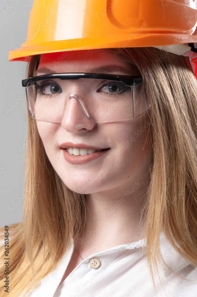 Portrait of a young attractive woman with blond hair in orange helmet on a neutral gray background. Portrait of a young attractive woman with blond hair in orange helmet on a neutral gray background.