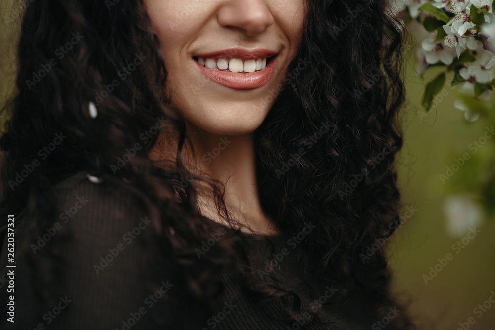 Portrait of a beautiful curly woman, smiling in the forest behind tree flowers in the middle of a spring day Portrait of a beautiful curly woman, smiling in the forest behind tree flowers in the middle of a spring day
