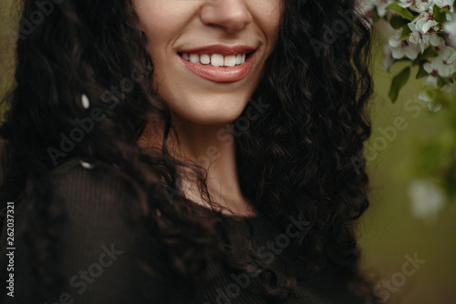 Portrait of a beautiful curly woman, smiling in the forest behind tree flowers in the middle of a spring day © Blume