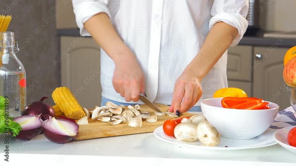 Close-up of a young woman's hand cutting vegetables in the kitchen with a knife on the table. She cuts fresh mushrooms. Close-up of a young woman's hand cutting vegetables in the kitchen with a knife on the table. She cuts fresh mushrooms.