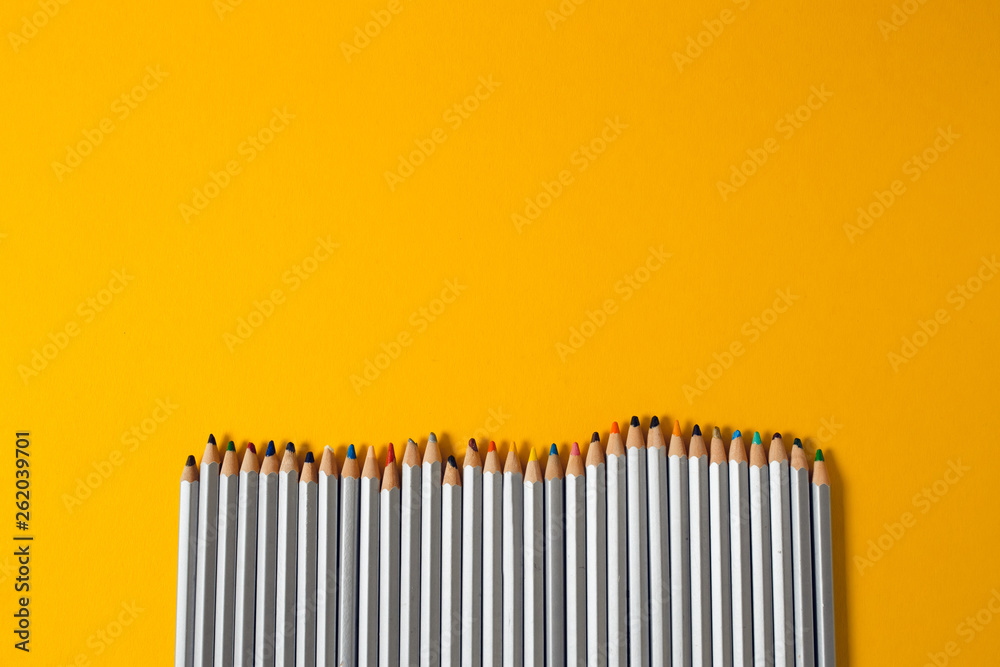 colored pencils arranged in a chaotic line on yellow background colored pencils arranged in a chaotic line on yellow background