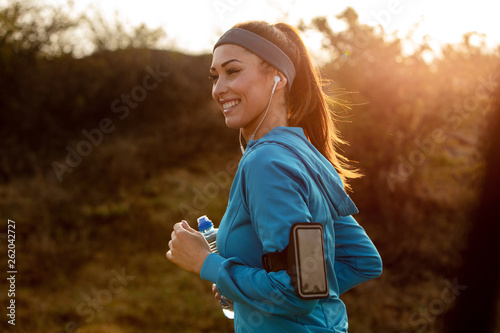 Happy female athlete jogging at dawn in nature. © Drazen