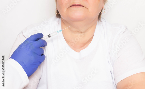 The doctor makes hyaluronic acid injections and lipofilling for an aged woman in a double chin  getting rid of wrinkles  rejuvenation  white background  problems
