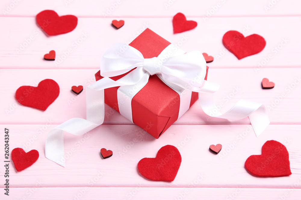 Gift box with ribbon bow and red hearts on pink wooden table