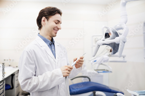 Side view portrait of young dentist setting up equipment in office and smiling  copy space