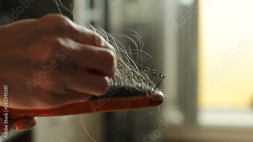 A woman's hand holding a comb with hair. The concept is the problem of hair loss. Close-up of slow motion