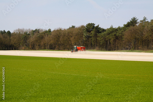 ROERMOND, NETHERLANDS - MARCH 30. 2019: Chalk fertilizer application by tractor with spreader to prepare the field for growing grass lawn photo