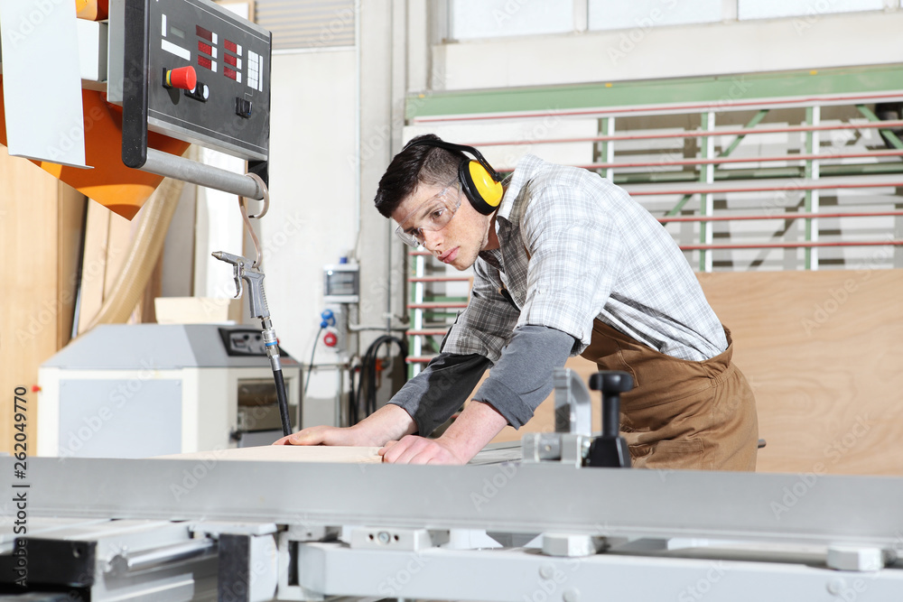 carpenter man work in the joinery, cut a wooden board with circular saw machine, protected with ear muffs and glasses carpenter man work in the joinery, cut a wooden board with circular saw machine, protected with ear muffs and glasses