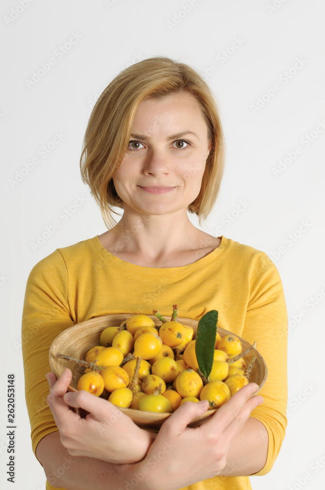 woman in yellow shirt holding in her arms a bowl with chinese spring yellow fruit, loquat, over white background woman in yellow shirt holding in her arms a bowl with chinese spring yellow fruit, loquat, over white background