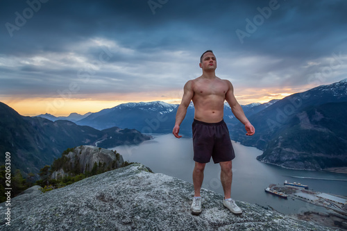 Fit and Muscular Young Man is on top of the Mountain during a cloudy sunset. Taken on Chief Mountain in Squamish, North of Vancouver, BC, Canada.