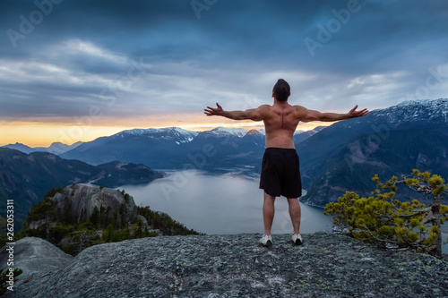 Fit and Muscular Young Man is on top of the Mountain during a colorful sunset. Taken on Chief Mountain in Squamish, North of Vancouver, BC, Canada.