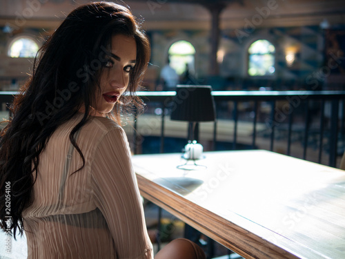 beautiful brunette model sitting on the couch at the table indoors turning back and looking at the camera