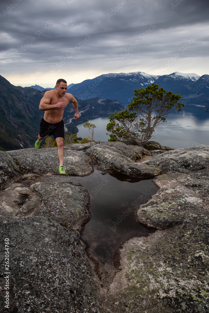 Fit and Muscular Young Man is Running up the Mountain during a cloudy day. Taken on Chief Mountain in Squamish, North of Vancouver, BC, Canada. Fit and Muscular Young Man is Running up the Mountain during a cloudy day. Taken on Chief Mountain in Squamish, North of Vancouver, BC, Canada.