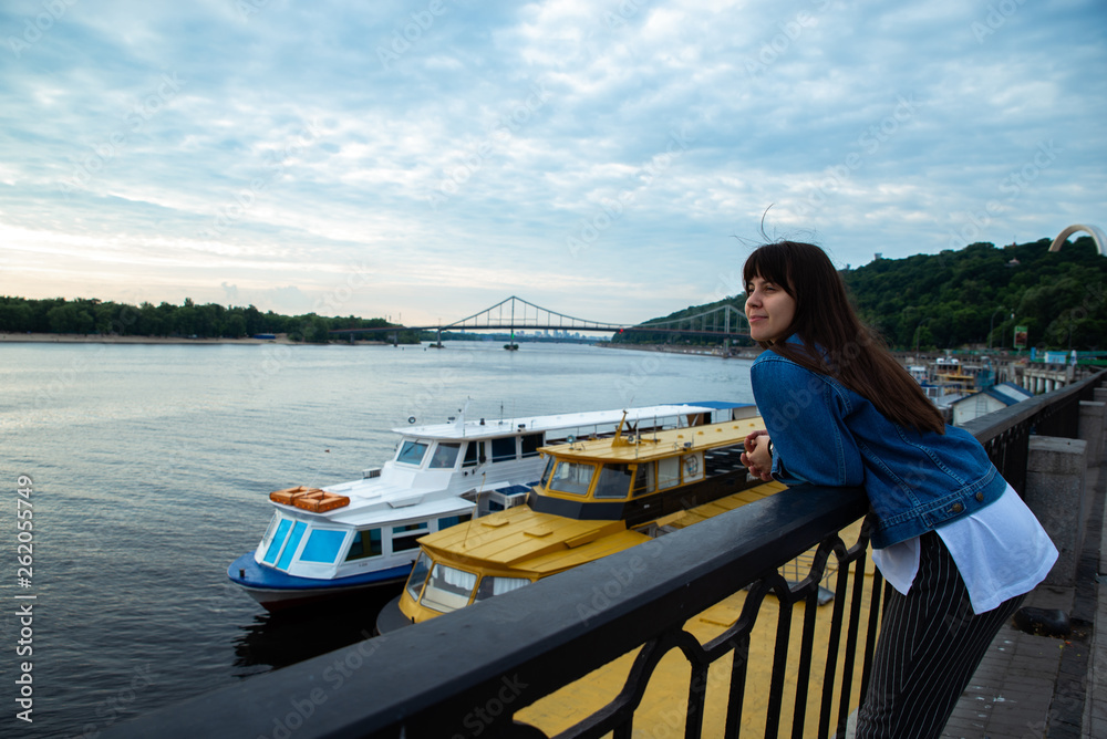 young pretty woman looking on river at morning time. boats in dock