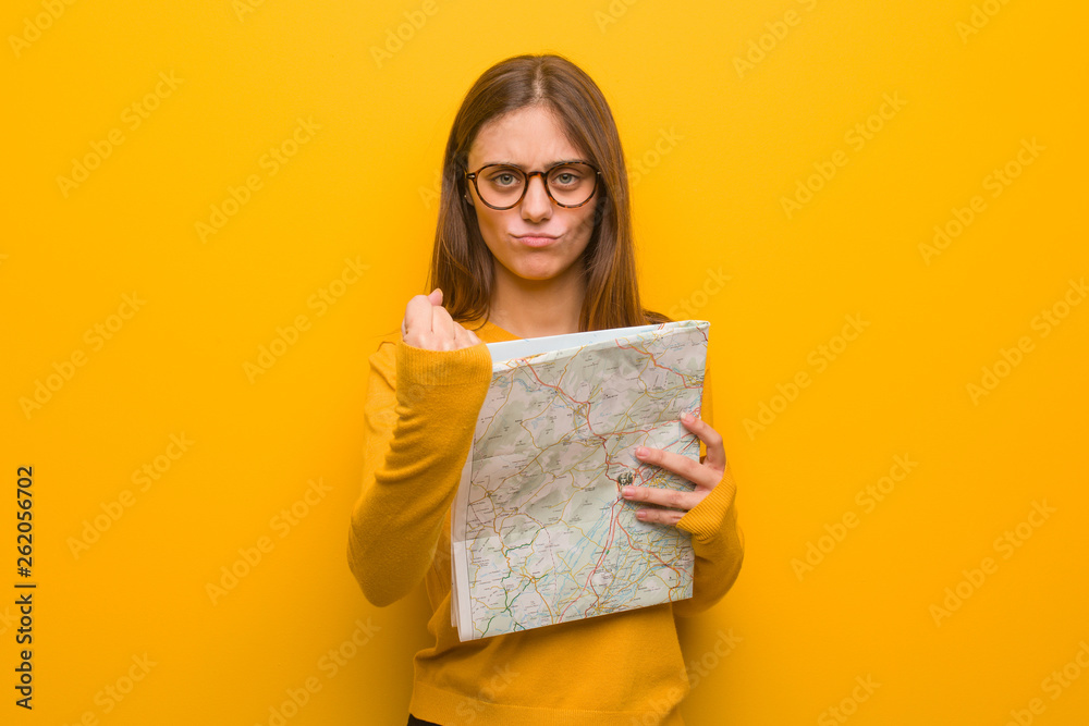 Fototapeta premium Young pretty caucasian woman showing fist to front, angry expression. She is holding a map.