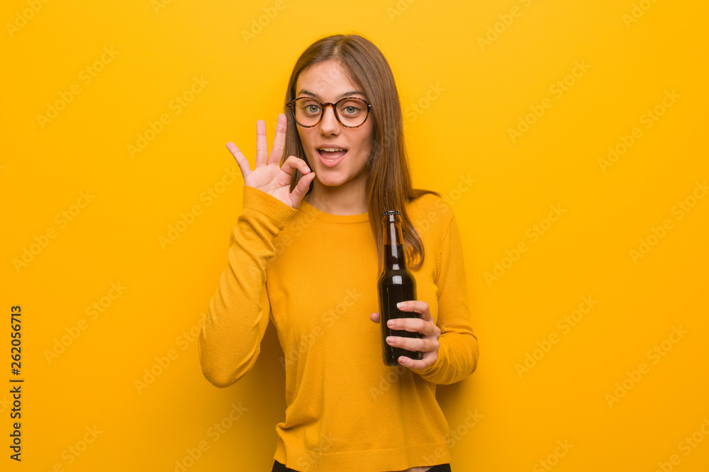 Young pretty caucasian woman cheerful and confident doing ok gesture. She is holding a beer. Young pretty caucasian woman cheerful and confident doing ok gesture. She is holding a beer.