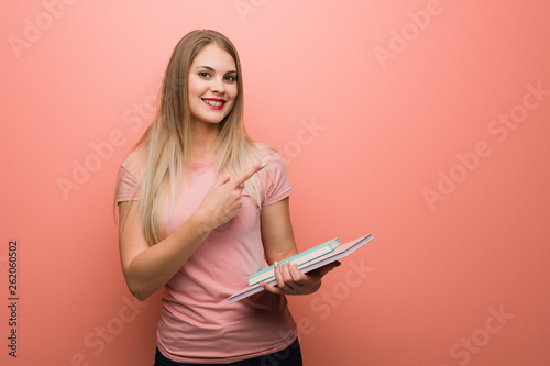 Young pretty russian girl pointing to the side with finger. She is holding books.